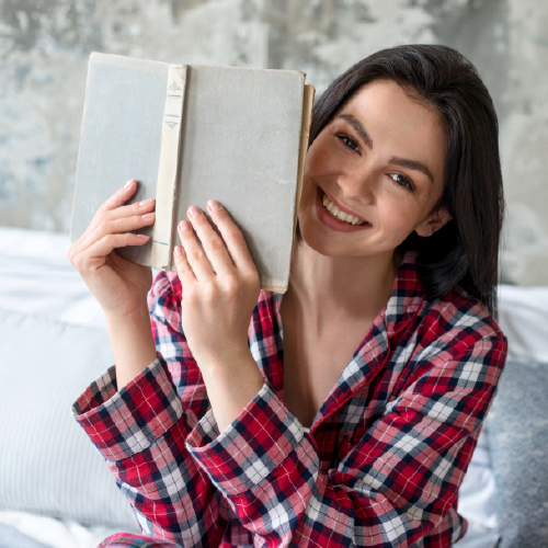 chica sonriente sosteniendo un libro abierto con ambas manos al lado de su cara